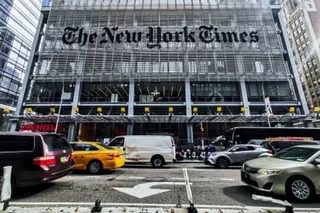 The New York Times building facade with Gothic lettering above a busy Manhattan street with yellow taxis