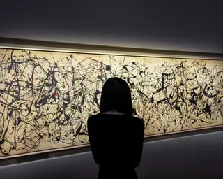 A woman is silhouetted in front of a large canvas of drips and swirls of black paint punctuated by spots of red