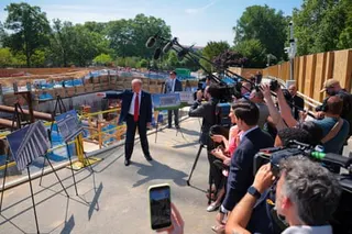 Donald Trump gestures toward construction site while speaking to media and cameras at an outdoor event