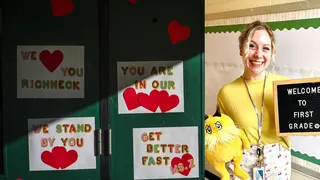 Teacher Abby Zwerner holding a sign and smiling in front of a door with get well soon messages at Richneck Elementary School