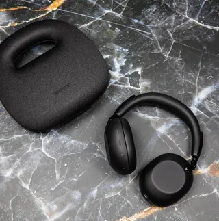 The Sony 1000X The Collexion headphones next to their carrying case on a marble surface.