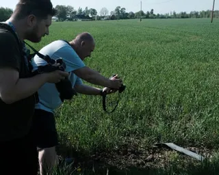Two men take photos of a piece of metal in a field