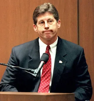 Detective Mark Fuhrman in a dark suit and red polka-dot tie sits at a witness stand with a microphone