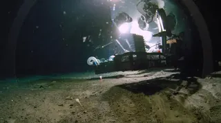 一艘載人潛水器懸浮於陰暗的海底上方，周圍瀰漫細緻的沉積物