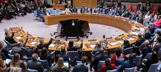 联合国安理会会议室的广角照片显示成员国会议讨论中东局势, 几位代表举手.