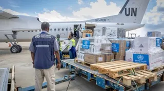 World Health Organization workers moving crates of supplies by a plane.