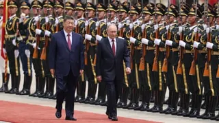 Vladimir Putin and Xi Jinping walk down a red carpet past soldiers.