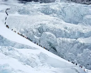 A long line of climbers ascends a snowy Mount Everest ridge above a heavily crevassed glacier