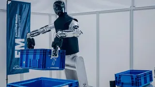 An industrial robot with a wheeled base lifting a crate.