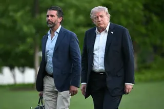 Donald Trump and Donald Trump Jr. walk across a lawn with trees in the background