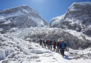 A line of people walk up a glacier on a sunny day
