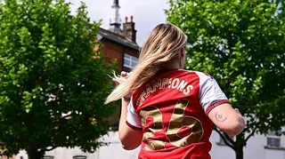 Female Arsenal fan with 'Champions 26' on the back of her shirt