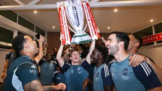 Arsenal players happy and celebrating in football kit lifting a trophy above their heads