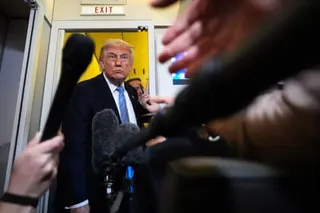 a man in suit stands on aircraft and looks at people holding microphones in his direction