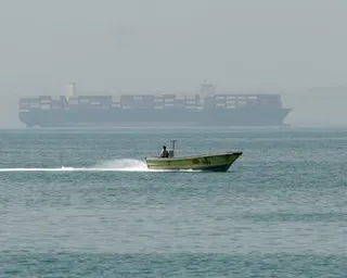 Container ship on the horizon with small motorboat in foreground