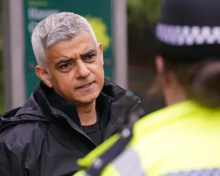 Mayor of London Sadiq Khan in a black jacket speaks to someone in a high-visibility vest outdoors