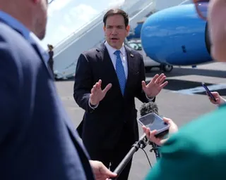 Secretary of State Marco Rubio speaks to reporters holding recording devices on an airport tarmac