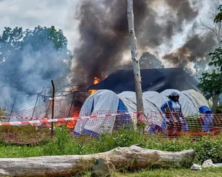 Smoke rises from a building, with tents and a plastic cordon in the foreground