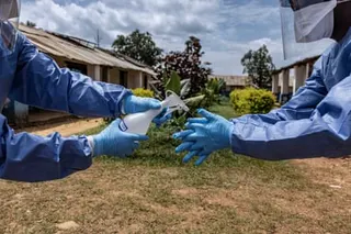 A health workers wearing protective equipment sprays disinfectant on another’s gloved hands
