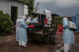 A group of medical staff wearing full-body protective equipment spray the trailer with disinfectant