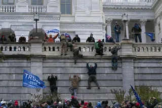 People climb a wall and wave Trump flags.