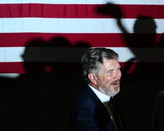 man in suit smiles with american flag in background