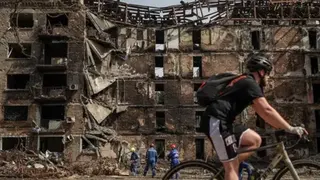 Reuters A cyclist rides past a damaged building, with a crew cleaning up in front of it