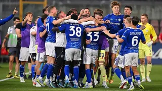 Como players, in blue shirts and socks and white shorts, celebrate in a huddle after securing Champions League qualification