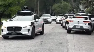 A litany of Waymo cars take up all the space in a street.