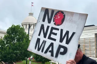 a demonstrator holds a placard opposing gerrymandering stating 'no new map'