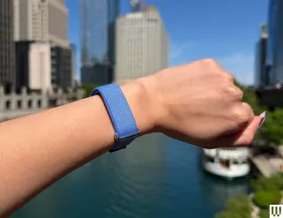 A person's wrist wearing a blue band with a city skyline and river in the background