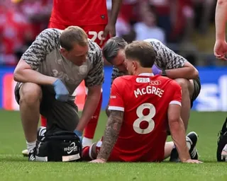 Footballer Riley McGree sits on the pitch receiving attention from two medical staff members during a match