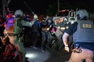 Officers in tactical gear strike protesters with batons during a nighttime confrontation near a truck