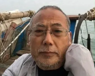 Dong takes a selfie on a boat with ropes and water visible behind him