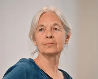 Daniela Klette: she is 67 with long, straight grey hair tied back from her face. She wears a blue top and looks defiantly into the camera.