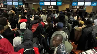 A group of people look at bright information boards inside an airport terminal.