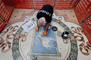 Restorer Gianluca Galli works on the mosaic of the bull during the restoration in the Galleria Vittorio Emanuele II, Milan, Italy on Thursday. Photo:  AFP