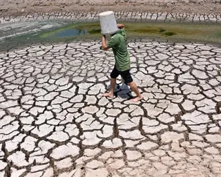 Person with bucket on head walks across cracked mud