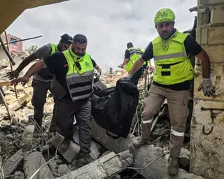Civil defence members carrying body in bag amid rubble