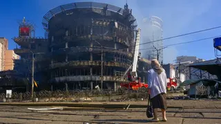一位戴著頭巾的​​女子背對著鏡頭，注視著消防員撲滅一座大型圓形建築的火災——可以看到濃煙升騰入天空