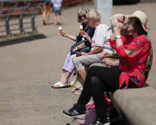 Four older women sit on a low stone wall and eat ice creams on the promenade at Blackpool.