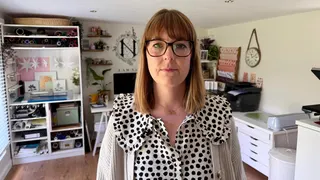 Natalie Ramsell-Lee. She has short brown hair, a fringe and wears glasses. She is also wearing a black and white polkadot blouse. She is sat her desk, with one of her designs on the screen, and is smiling at the camera.