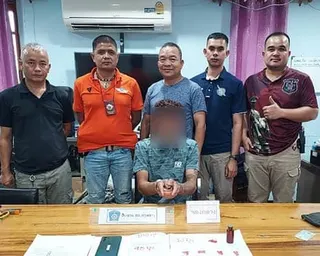 Five male police officers, dressed in T-shirts and trousers, stand behind a man in handcuffs whose faced is blurred
