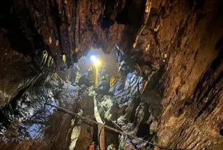 EPA An enormous rocky cavern fills the image with the centre showing the entrance to the cave and four rescuers dressed in blue outfits and helmets using a yellow pump hose, which stretches all the way to the bottom of the picture. A bright yellow light picks out the details of the craggy rocks inside the cave from where they are standing