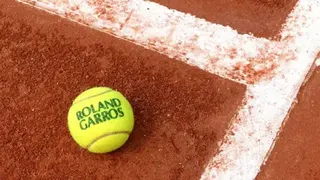 一個印有「ROLAND GARROS」字樣的網球，放在紅土網球場地面上