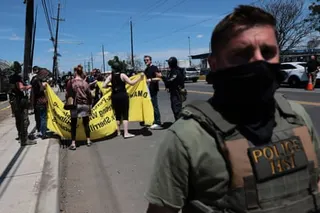 a man in a tactical vest stands near people holding a banner