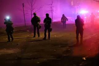 Federal agents stand on a street in a cloud of tear gas illuminated by red and blue lights