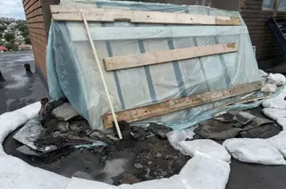 The site of a drone strike on a residential block roof covered with wood panels and blue plastic.