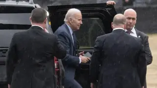 Getty Images Biden steps out of a black car in the rain surrounded by minders