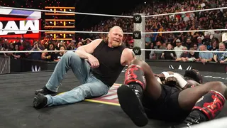 Brock Lesnar smiling while looking at Oba Femi lying on the mat during wrestling match